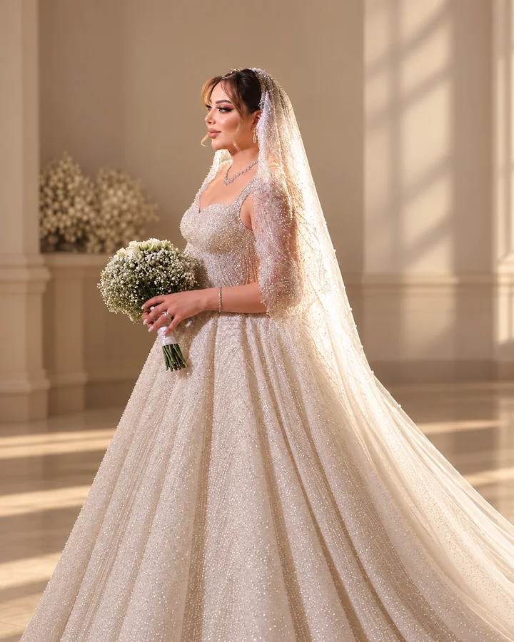 Bride in a beaded gown holding a bouquet, photographed in warm architectural surroundings